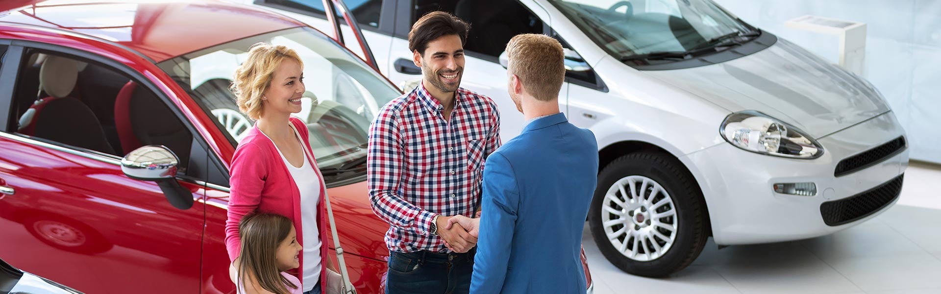 Two people shaking hands in front of a car